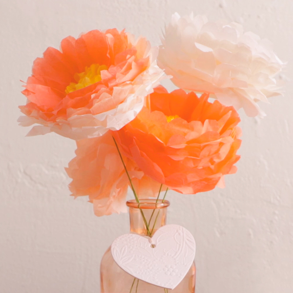 Um vaso cheio de flores diy com papel de seda laranja e branco.