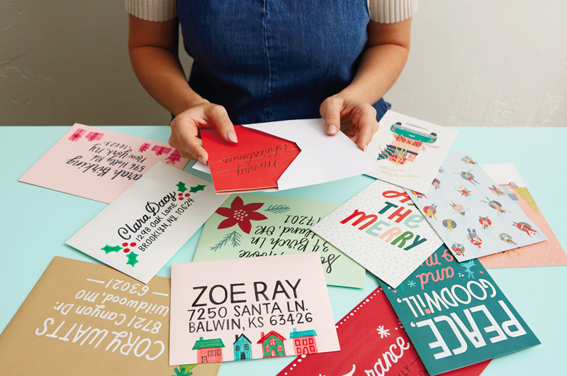 Uma mulher sentada em uma mesa coberta com um cartão de Natal e um envelope vividamente decorado.