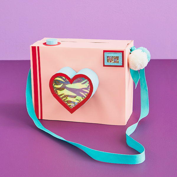 Câmera em forma de caixa de namorados com alça e lente em forma de coração.