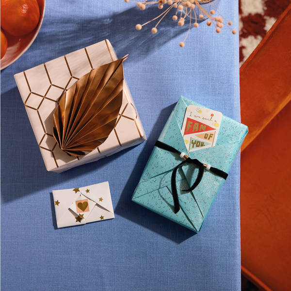 Três presentes embrulhados em um estilo inspirado na arte do origami estão sobre uma toalha de mesa azul ameixa.
