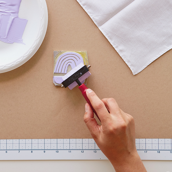 Mãos para aplicar tinta com um rolo no carimbo de borracha esculpida.