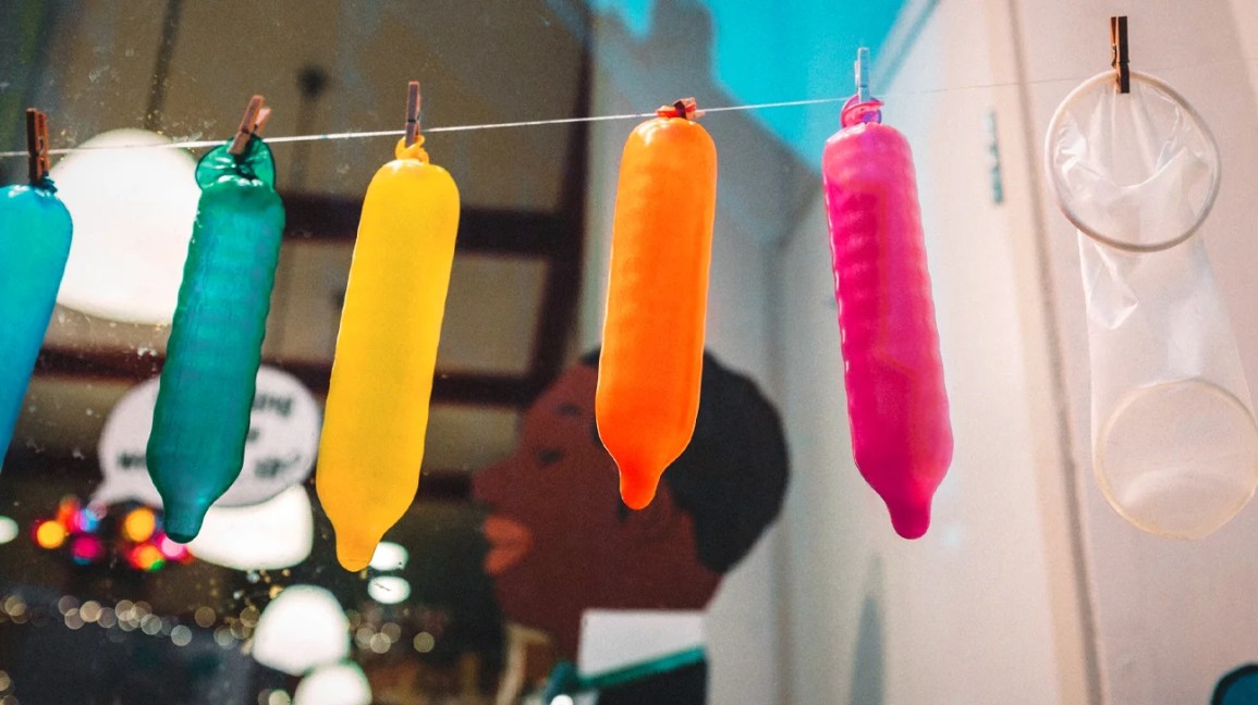 Quatro preservativos protuberantes de cores diferentes estão pendurados em uma corda fina.