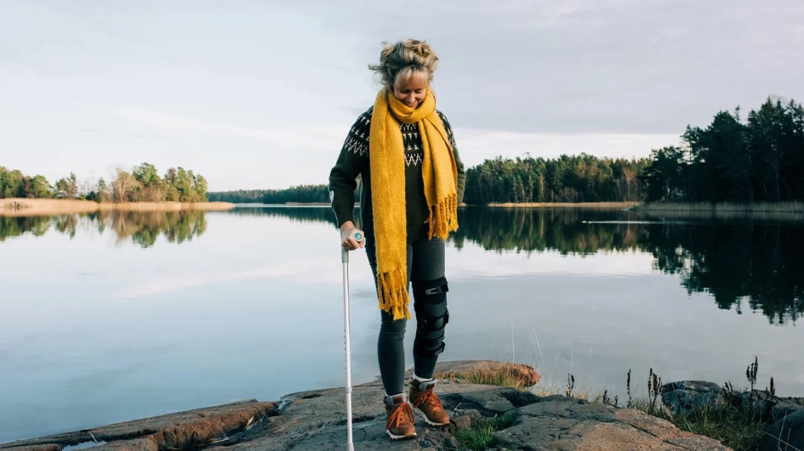 Fusão de tornozelo, mulher andando perto do lago com muletas